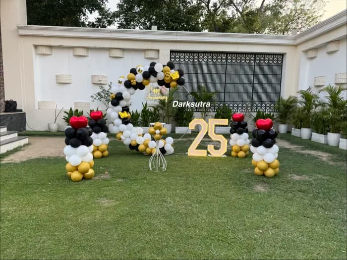 Outdoor garden balloon arch in black, gold and white with a light-up number 25 on a lawn
