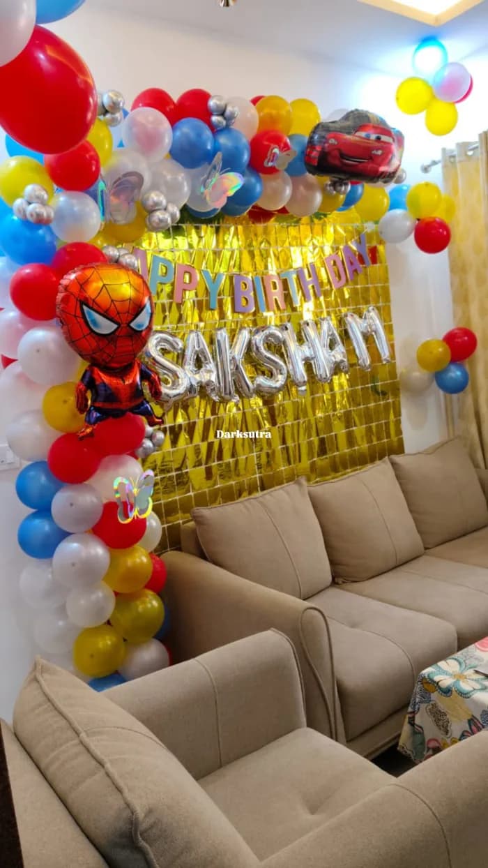 Superhero themed balloon arch in red, blue, yellow and white with a gold foil curtain and a personalised name in silver letters