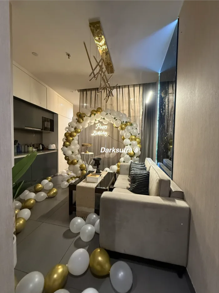 White and gold balloon arch with a neon Happy Birthday sign and a gold foil ceiling installation in a modern apartment