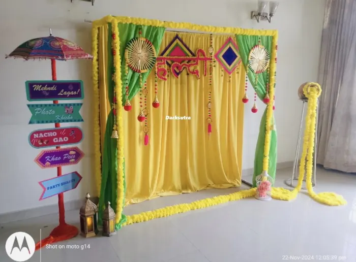 Yellow drape mehndi backdrop with marigold garlands, hand fans and a painted signboard with party phrases