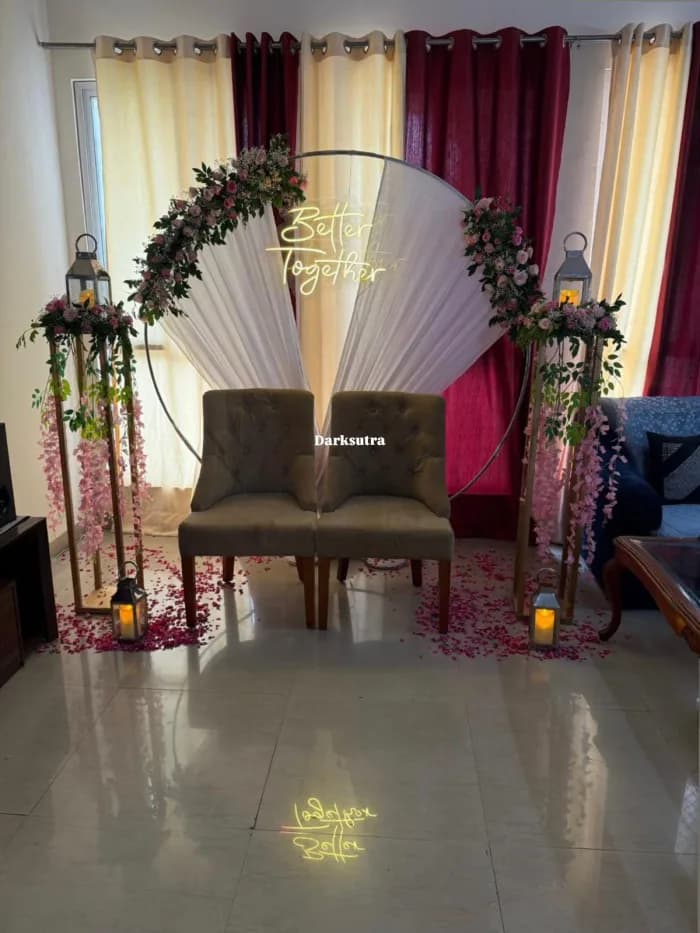 Round floral and drape arch with a neon Better Together sign, lanterns and two chairs on a rose petal aisle