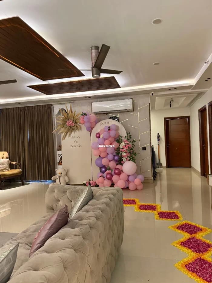 Pink and lilac balloon arch on a white welcome board with pampas grass and a teddy bear in a modern living room